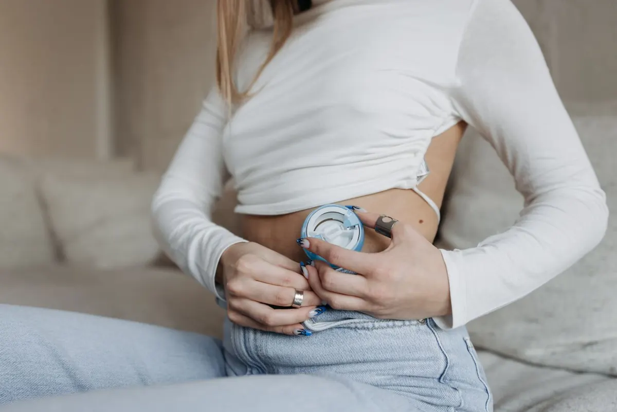 Una mujer sentada en el sofá se coloca una bomba de insulina en el abdomen.