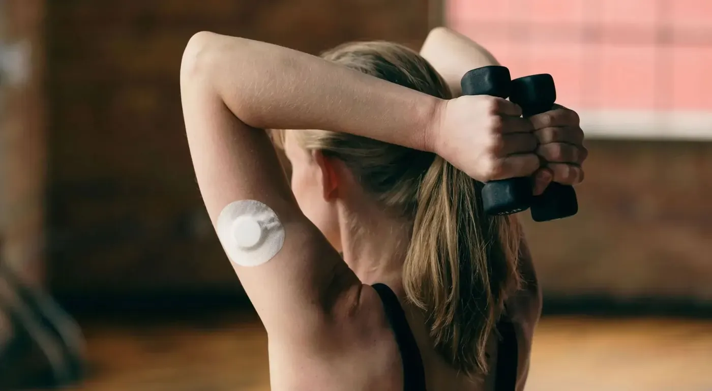 Una mujer entrena con mancuernas; lleva un sensor de glucosa en el brazo.